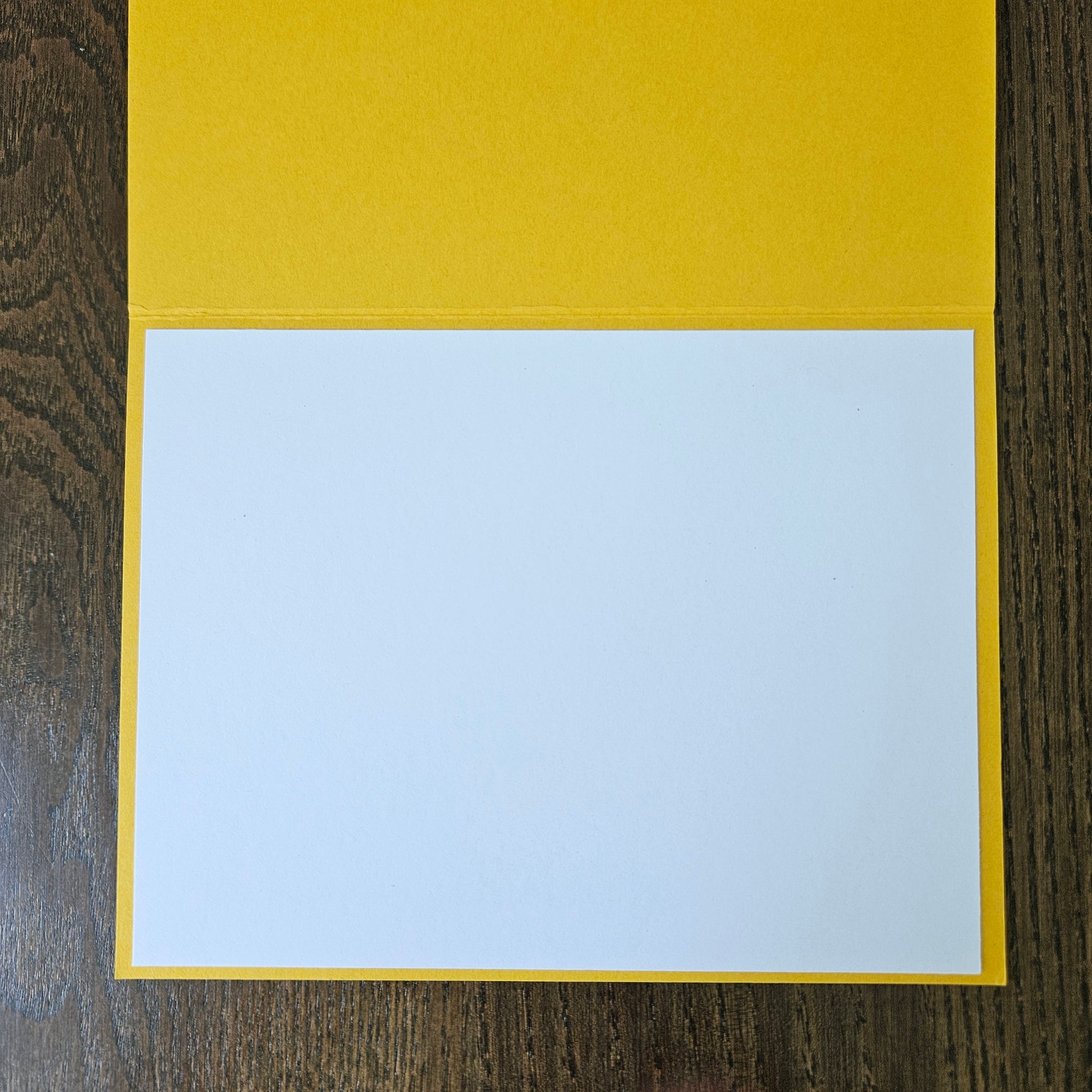 A blank white card or paper insert placed inside a bright yellow folder or envelope, photographed from above on a dark wood surface.