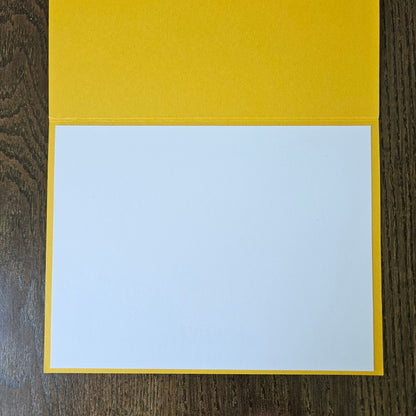 A blank white card or paper insert placed inside a bright yellow folder or envelope, photographed from above on a dark wood surface.