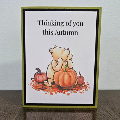 Front of a handmade A2 autumn card featuring classic Winnie the Pooh sitting with pumpkins and fall leaves framed by black and green borders with text reading Thinking of you this Autumn.