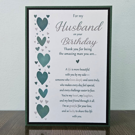 Front of a handmade 5x7 romantic birthday card for husband featuring a vertical row of teal hearts and layered green and black cardstock with printed text reading For my Husband on your Birthday.