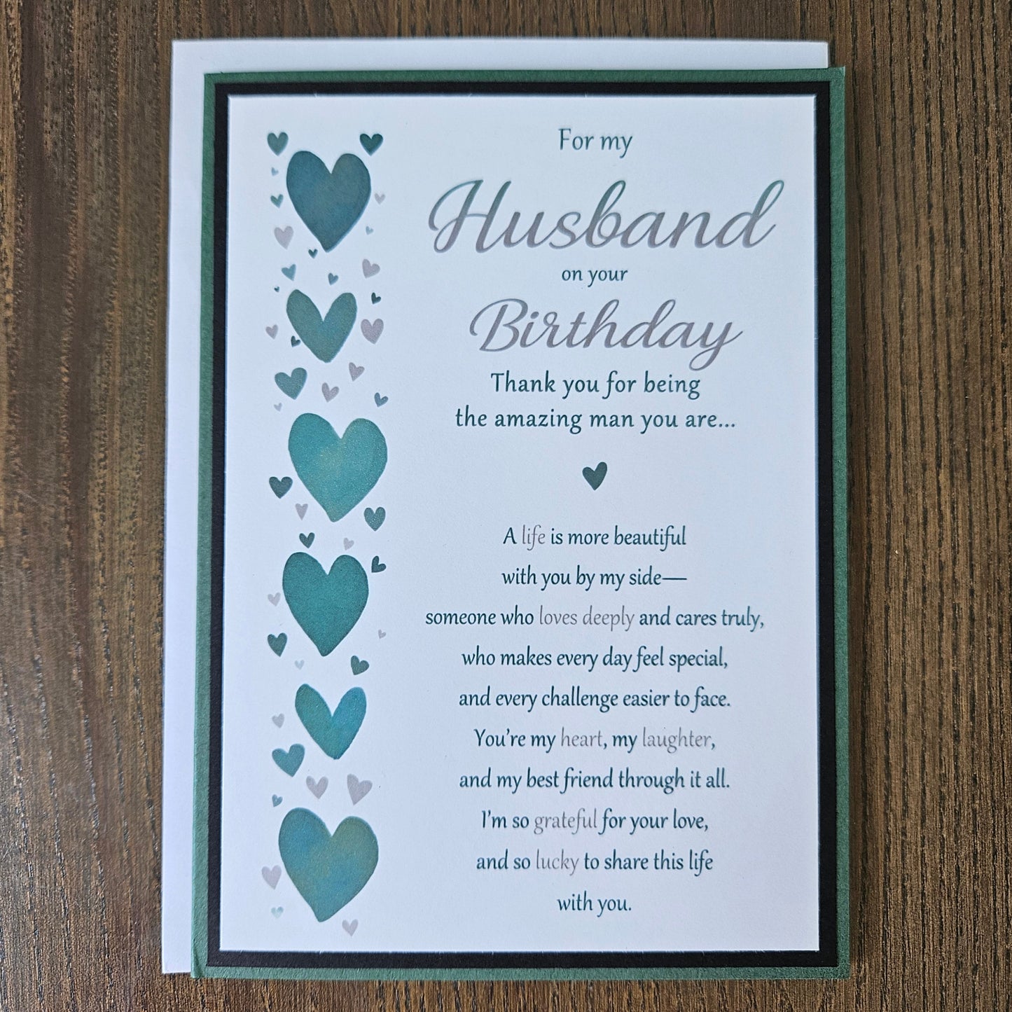 Front of a handmade 5x7 romantic birthday card for husband featuring a vertical row of teal hearts and layered green and black cardstock with printed text reading For my Husband on your Birthday.
