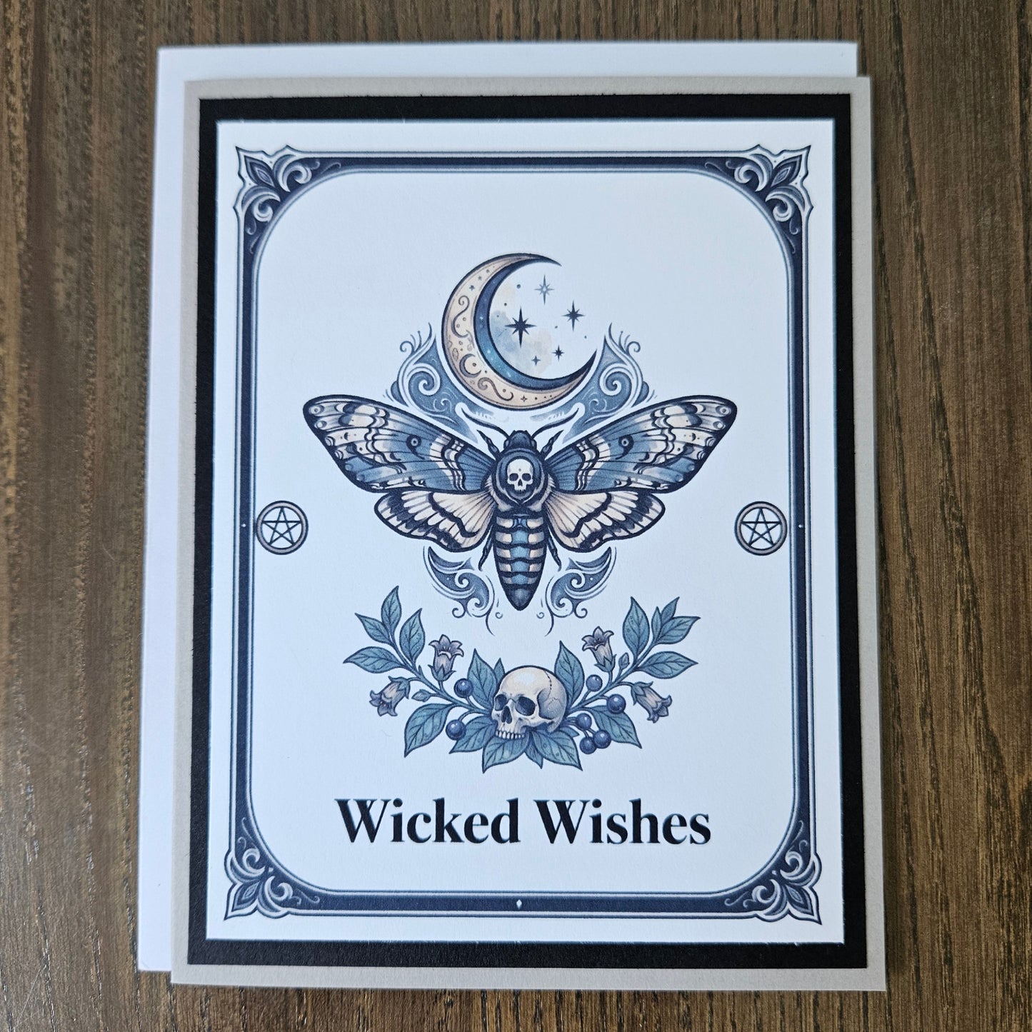 Front of a handmade A2 gothic card featuring a death head moth under a crescent moon with skulls and pentagrams framed in black and gray with text reading Wicked Wishes.