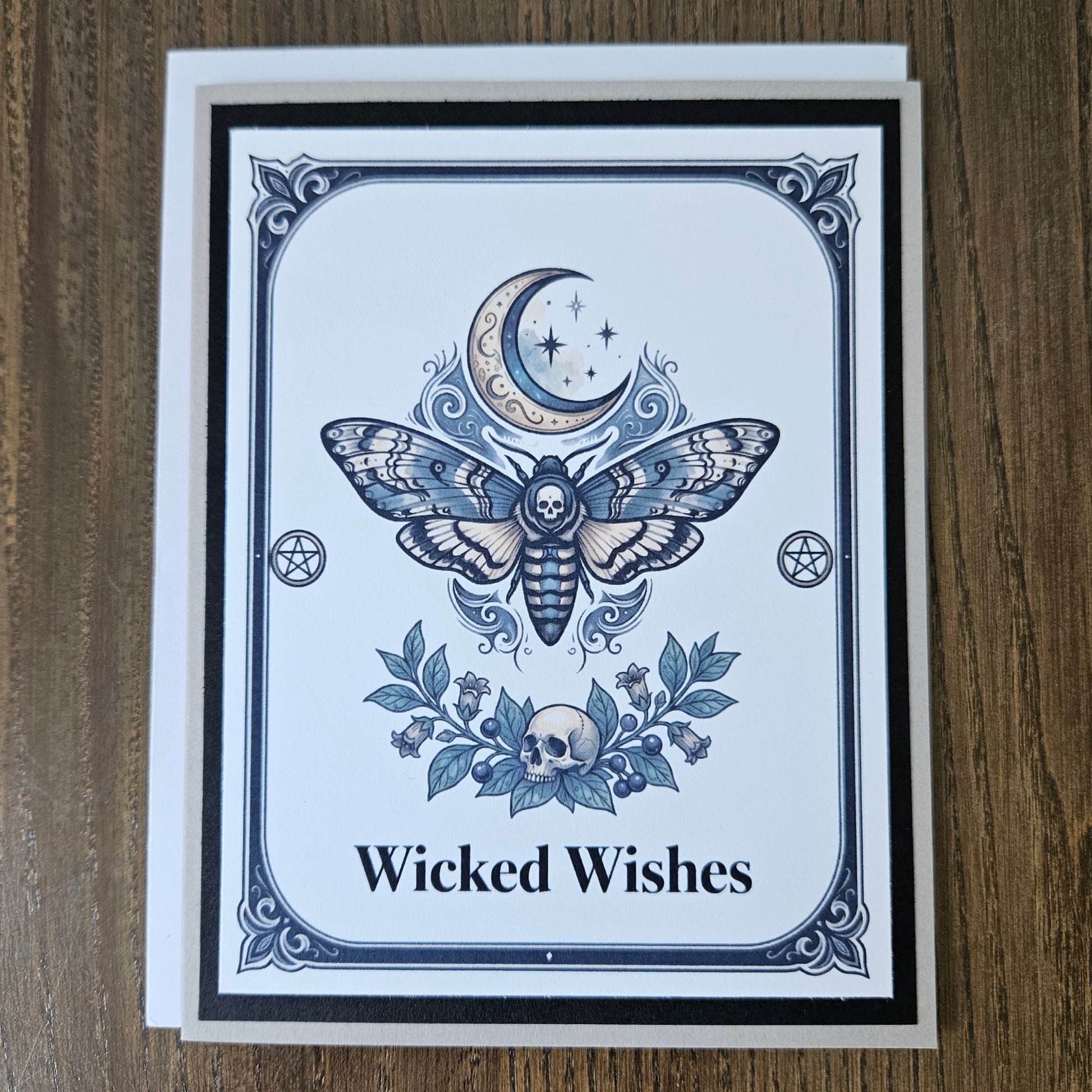 Front of a handmade A2 gothic card featuring a death head moth under a crescent moon with skulls and pentagrams framed in black and gray with text reading Wicked Wishes.