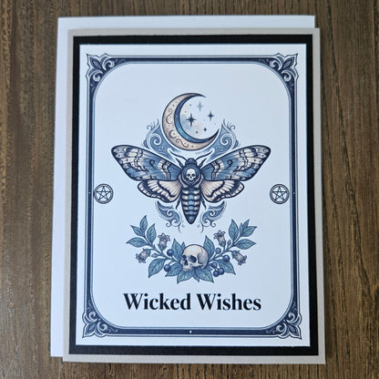Front of a handmade A2 gothic card featuring a death head moth under a crescent moon with skulls and pentagrams framed in black and gray with text reading Wicked Wishes.
