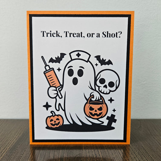 Front of a handmade A2 nurse Halloween card featuring a cute nurse ghost holding a syringe and pumpkin bucket framed by black and orange borders with text reading Trick Treat or a Shot.