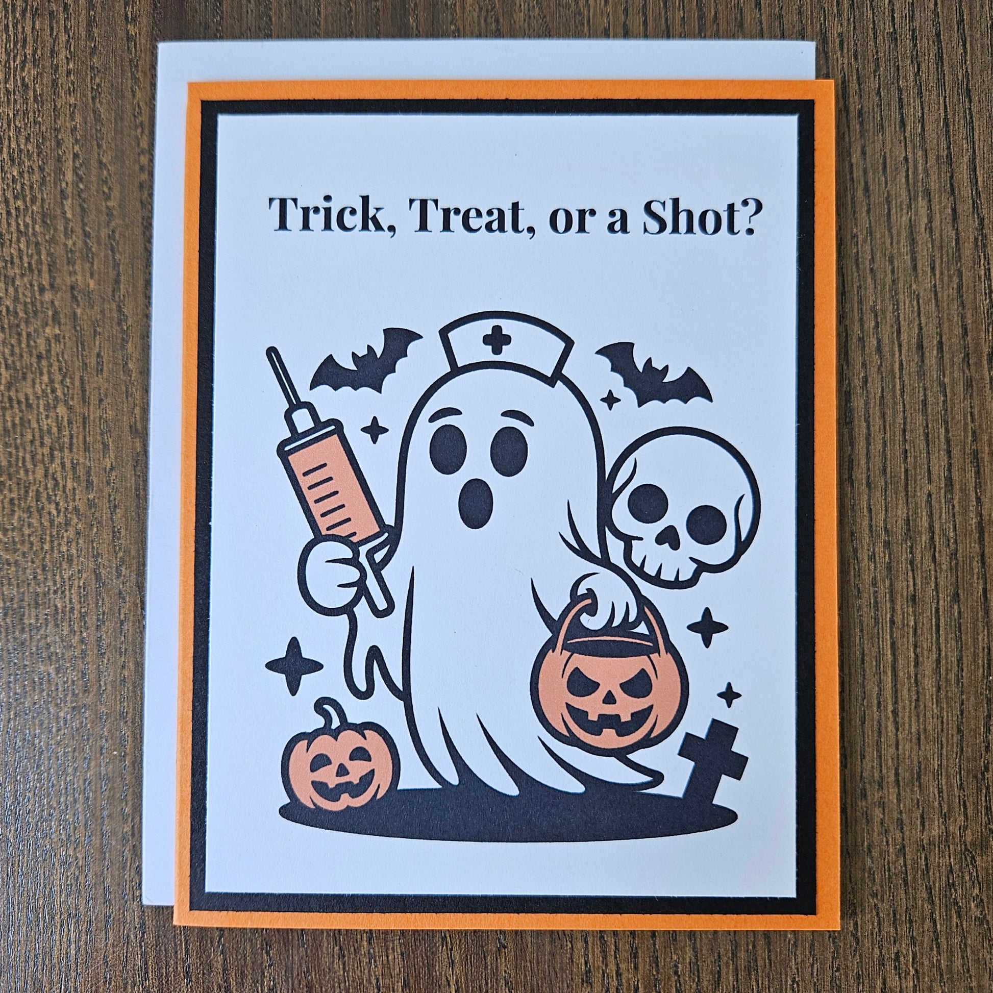 A square Halloween greeting card with an orange and black border, featuring a cartoon ghost holding a syringe and a jack-o'-lantern bucket, with the text 'Trick, Treat, or a Shot?' on a wooden tabletop.