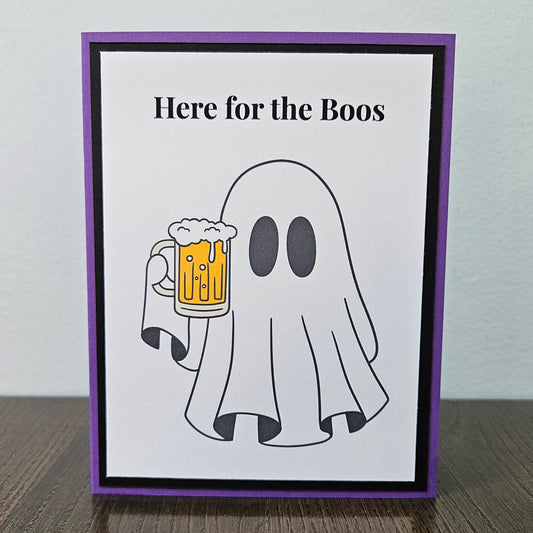 Front of a handmade A2 funny Halloween card featuring a ghost holding a beer mug framed by black and purple borders with text reading Here for the Boos.