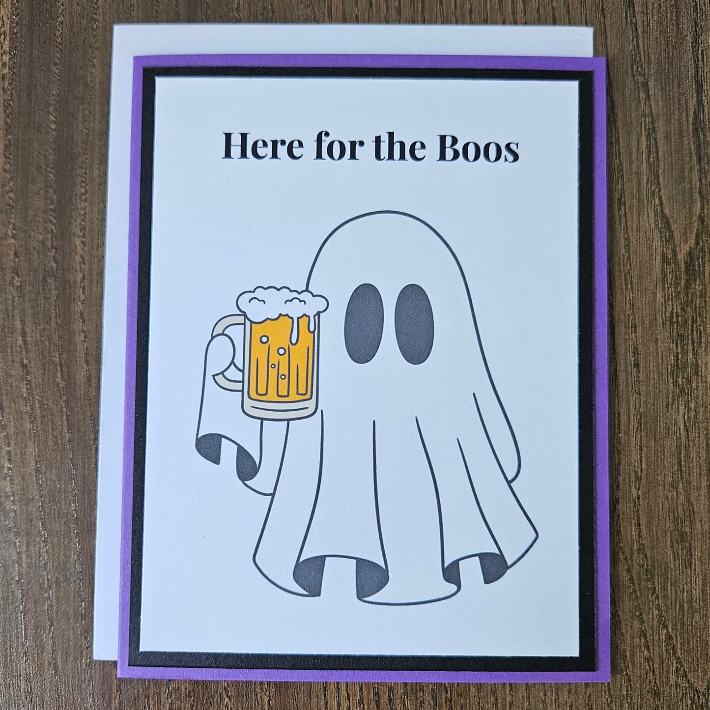 Front of a handmade A2 funny Halloween card featuring a ghost holding a beer mug framed by black and purple borders with text reading Here for the Boos.