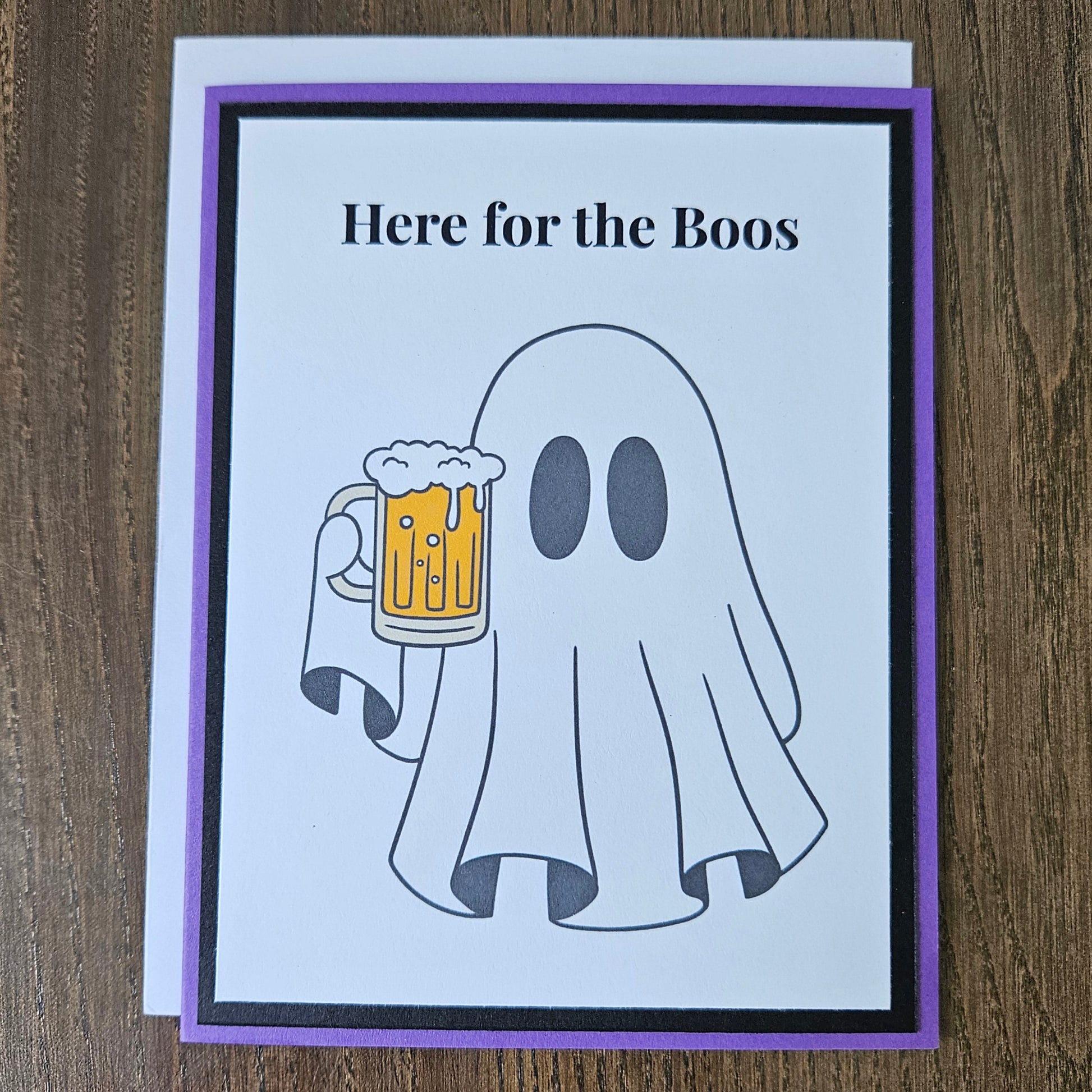 Front of a handmade A2 funny Halloween card featuring a ghost holding a beer mug framed by black and purple borders with text reading Here for the Boos.