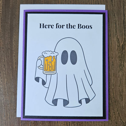 Front of a handmade A2 funny Halloween card featuring a ghost holding a beer mug framed by black and purple borders with text reading Here for the Boos.