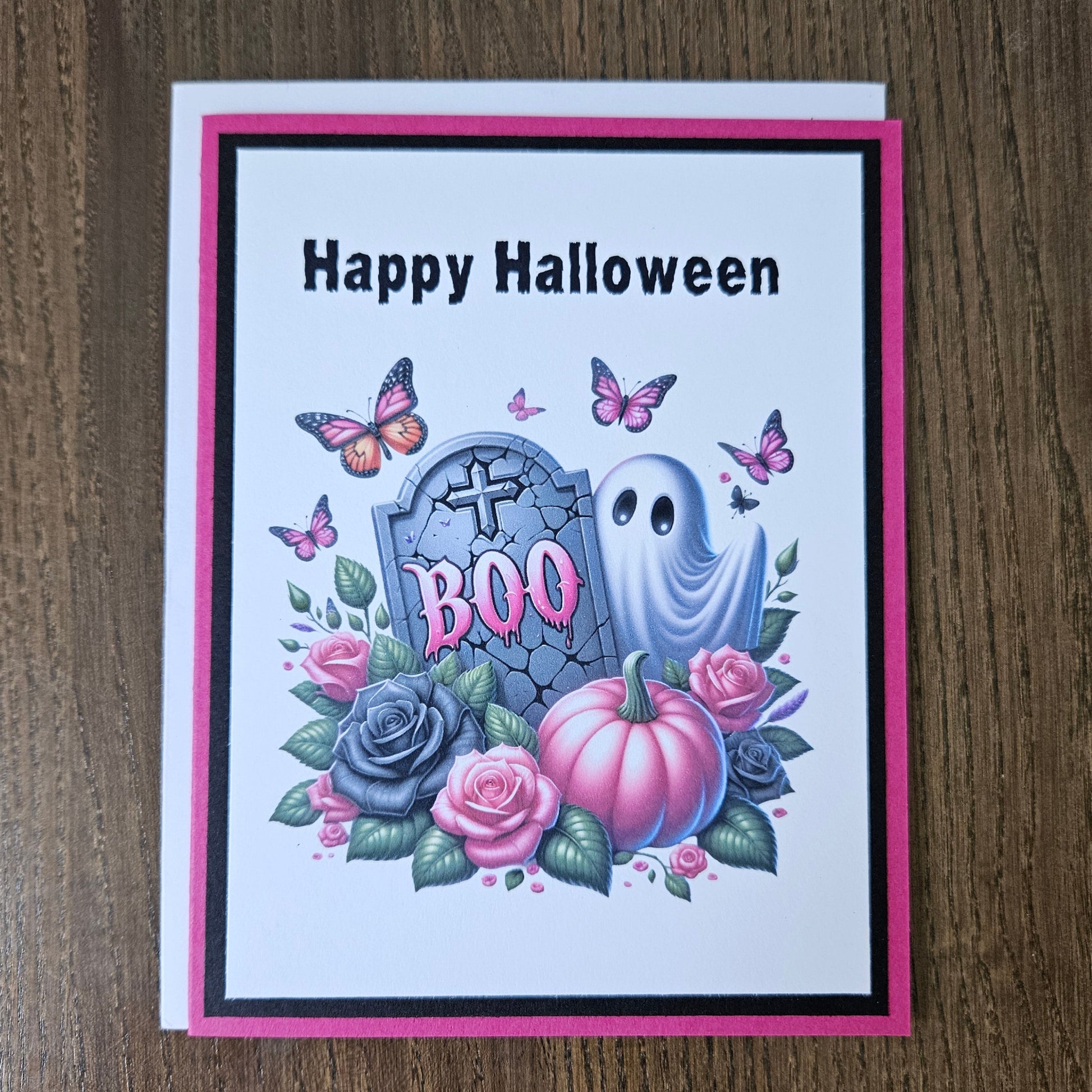 Front of a handmade A2 pastel goth Halloween card featuring a ghost, tombstone, pink pumpkin, roses, and butterflies framed in black and hot pink cardstock reading Happy Halloween.