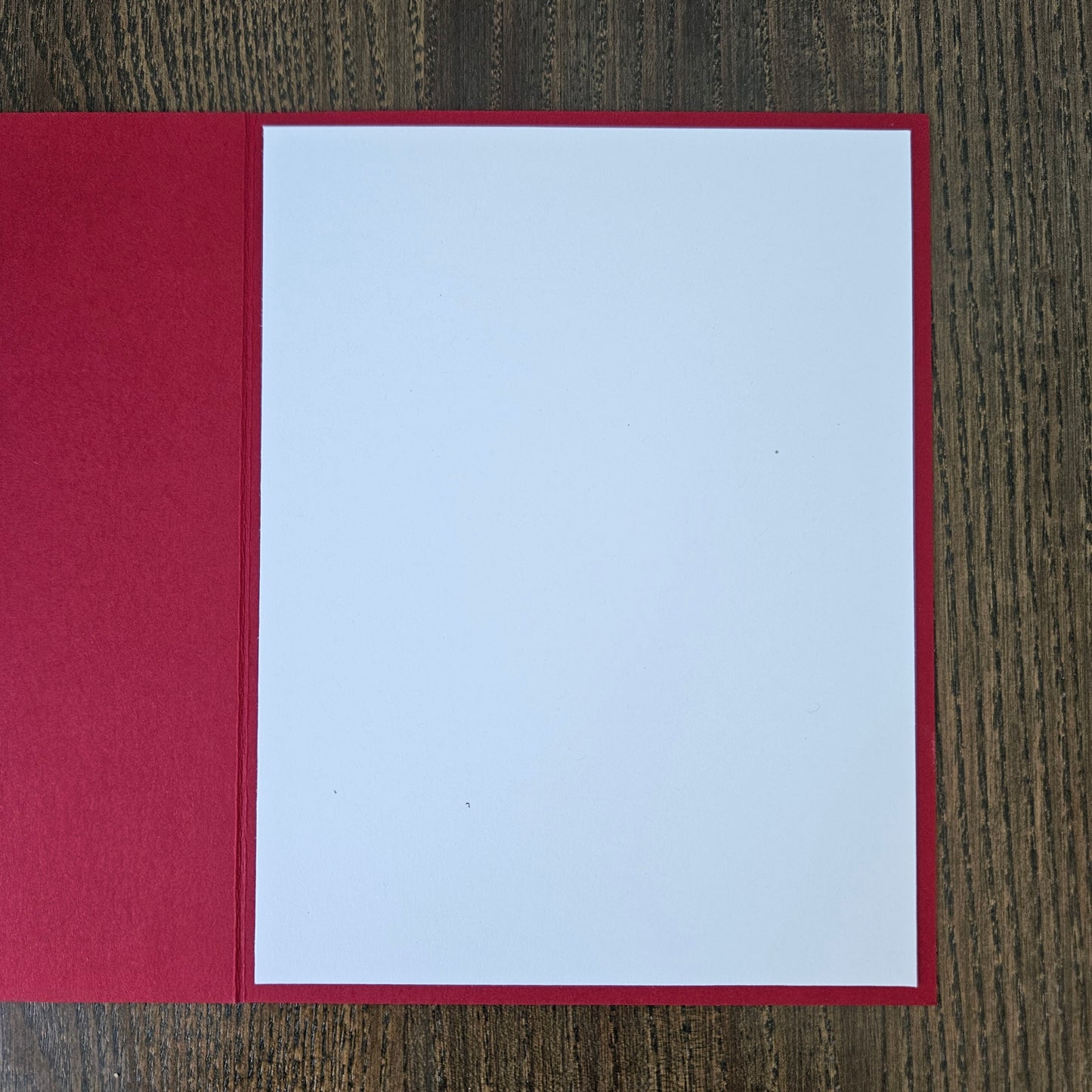 A blank white card or paper insert with a red border, displayed open on a dark wood grain surface.
