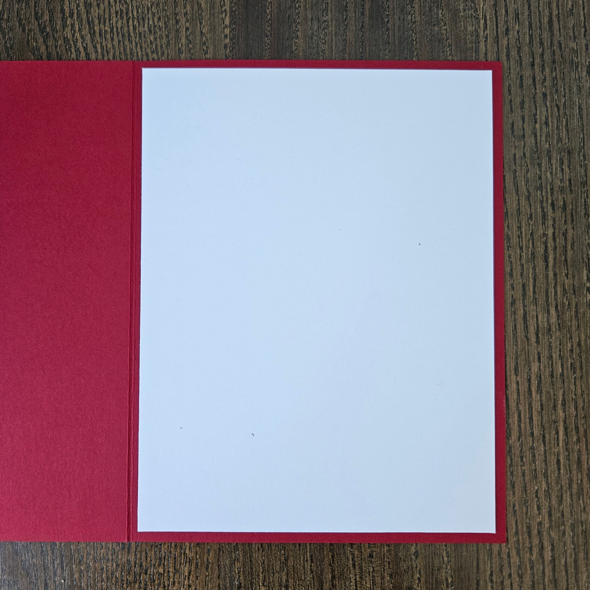 A blank white card or paper insert with a red border, displayed open on a dark wood grain surface.