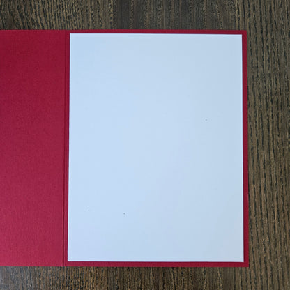 A blank white card or paper insert with a red border, displayed open on a dark wood grain surface.