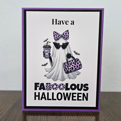 Front of a handmade A2 Halloween card featuring a layered purple and black border around a fashionable ghost wearing a purple leopard bow and sunglasses, holding an iced coffee and purse, with text reading Have a FABOOLOUS HALLOWEEN.