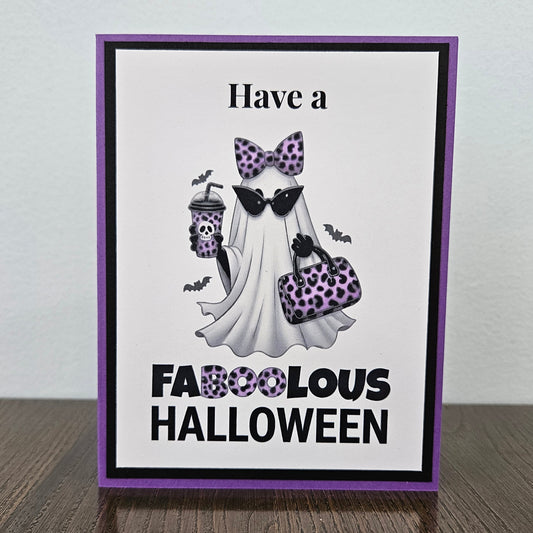 Front of a handmade A2 Halloween card featuring a layered purple and black border around a fashionable ghost wearing a purple leopard bow and sunglasses, holding an iced coffee and purse, with text reading Have a FABOOLOUS HALLOWEEN.