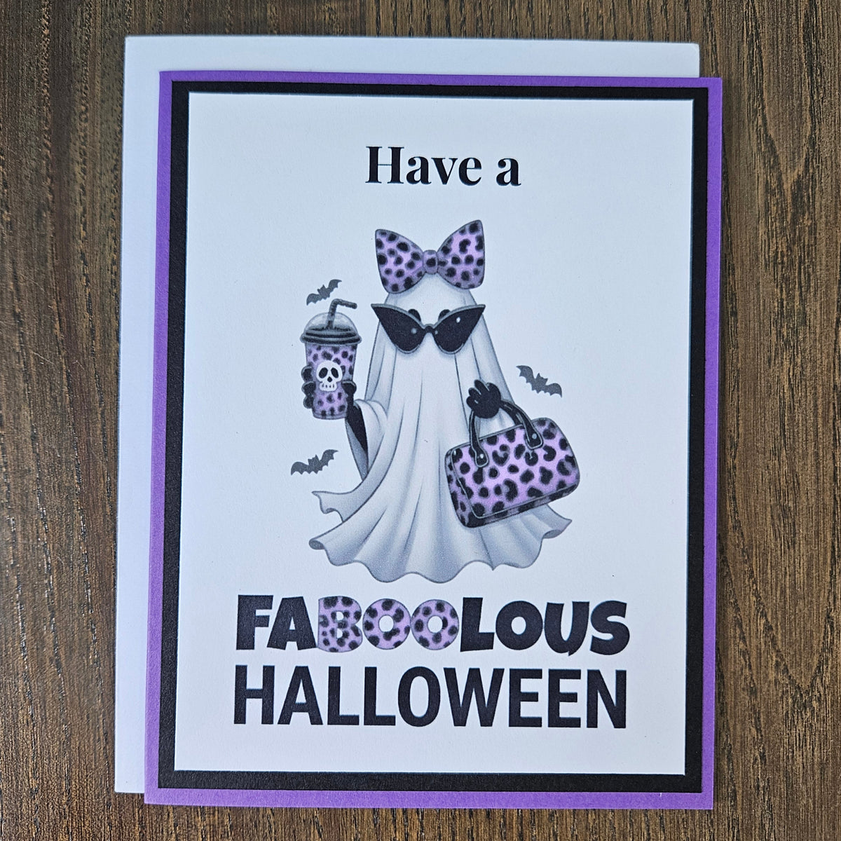 Front of a handmade A2 Halloween card featuring a layered purple and black border around a fashionable ghost wearing a purple leopard bow and sunglasses, holding an iced coffee and purse, with text reading Have a FABOOLOUS HALLOWEEN.
