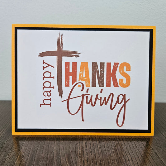 Front of a handmade A2 religious Thanksgiving card featuring a Christian cross integrated into text reading Happy Thanksgiving framed in black and yellow cardstock.
