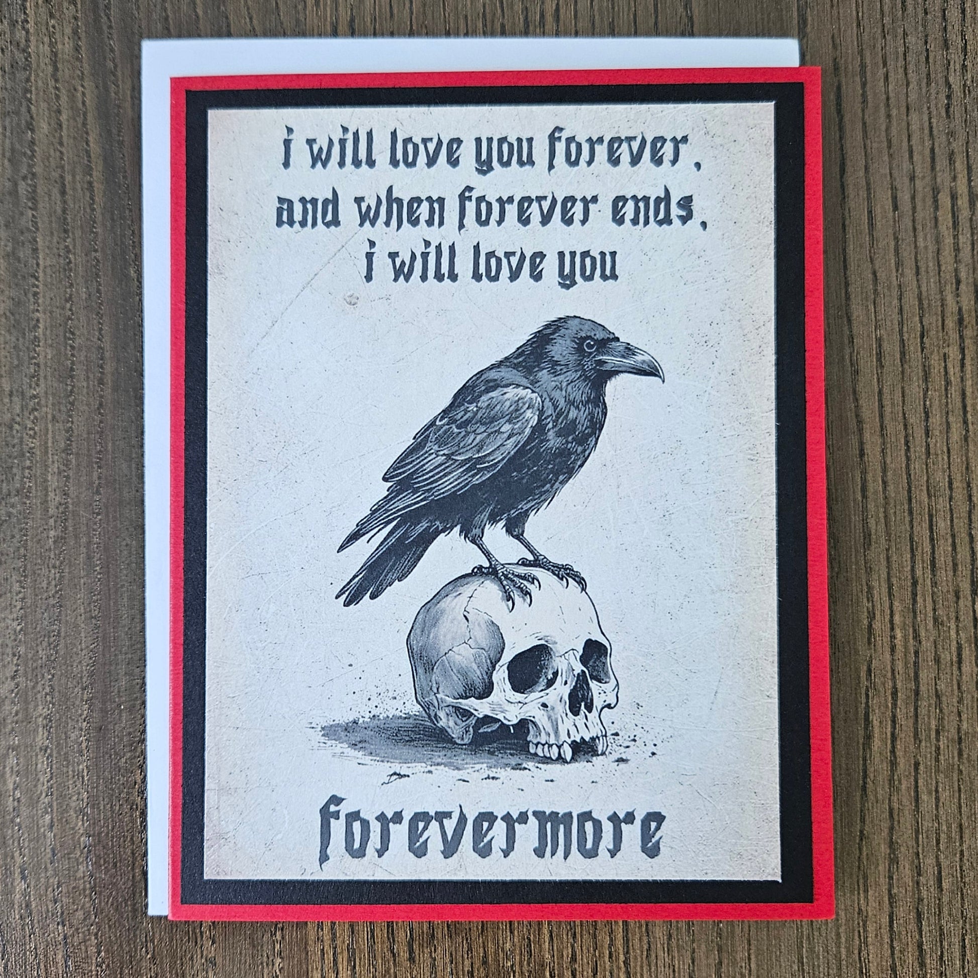 A square greeting card with a gothic design featuring a raven perched on a skull, with the text 'i will love you forever, and when forever ends, i will love you' and 'forevermore', displayed on a wooden surface.