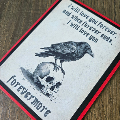 A square art print or card featuring a black raven perched on a skull, with gothic text reading 'I will love you forever and when forever ends, i will love you forevermore,' shown on a wood surface with a red and black border.