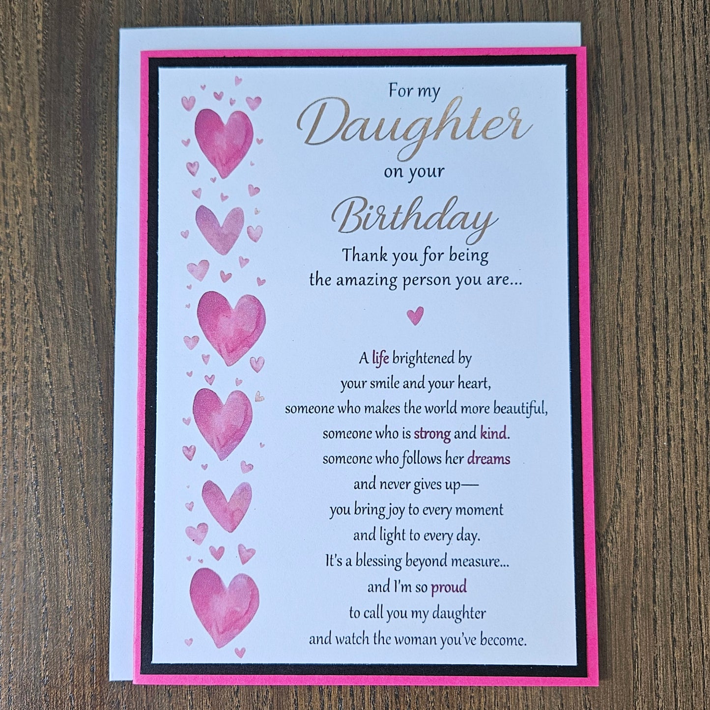Front view of a handmade 5x7 birthday card for daughter featuring pink watercolor hearts, bold black and hot pink borders, and printed sentimental verses.