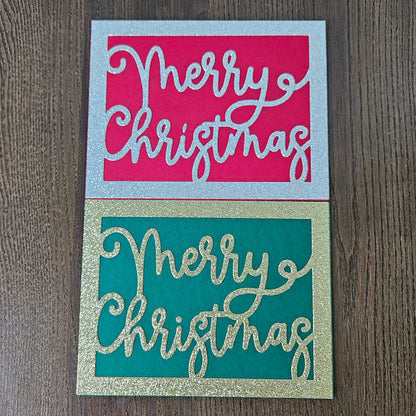 Two square Christmas greeting cards on a dark wood background. The top card has a silver glitter border with a bright pink center and white cursive text reading 'Merry Christmas.