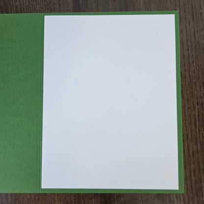 A blank white rectangular card or paper sheet placed on top of a green textured backing, photographed from above on a dark wood surface.
