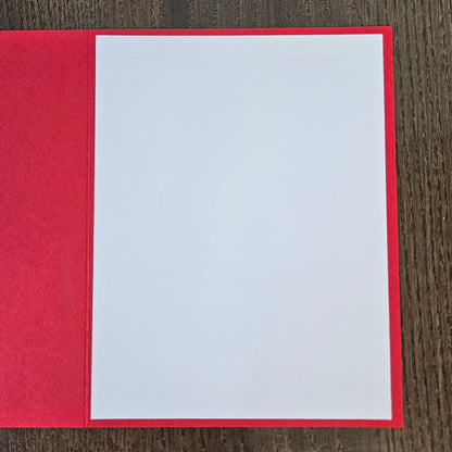 A red greeting card or notebook cover with a blank white insert page, photographed from above on a dark wood surface.