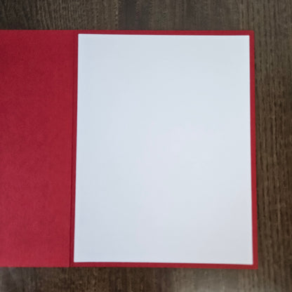 A blank white rectangular card or paper insert placed on top of a red textured cover, photographed from above on a dark wood surface.