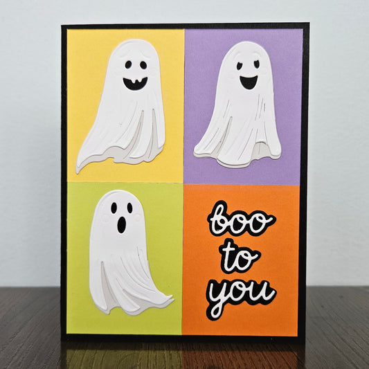 Front of a handmade A2 Halloween card featuring three cute white ghosts and Boo To You text on a colorful yellow, purple, green, and orange color-block background.