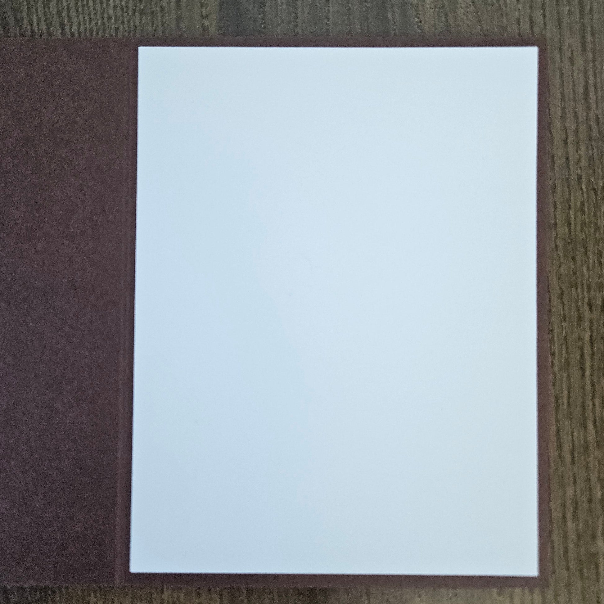A blank white rectangular card or paper sheet placed on top of a textured dark brown cover, photographed from above on a wood-grain surface.