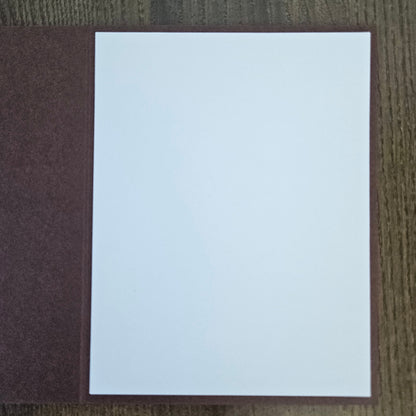 A blank white rectangular card or paper sheet placed on top of a textured dark brown cover, photographed from above on a wood-grain surface.