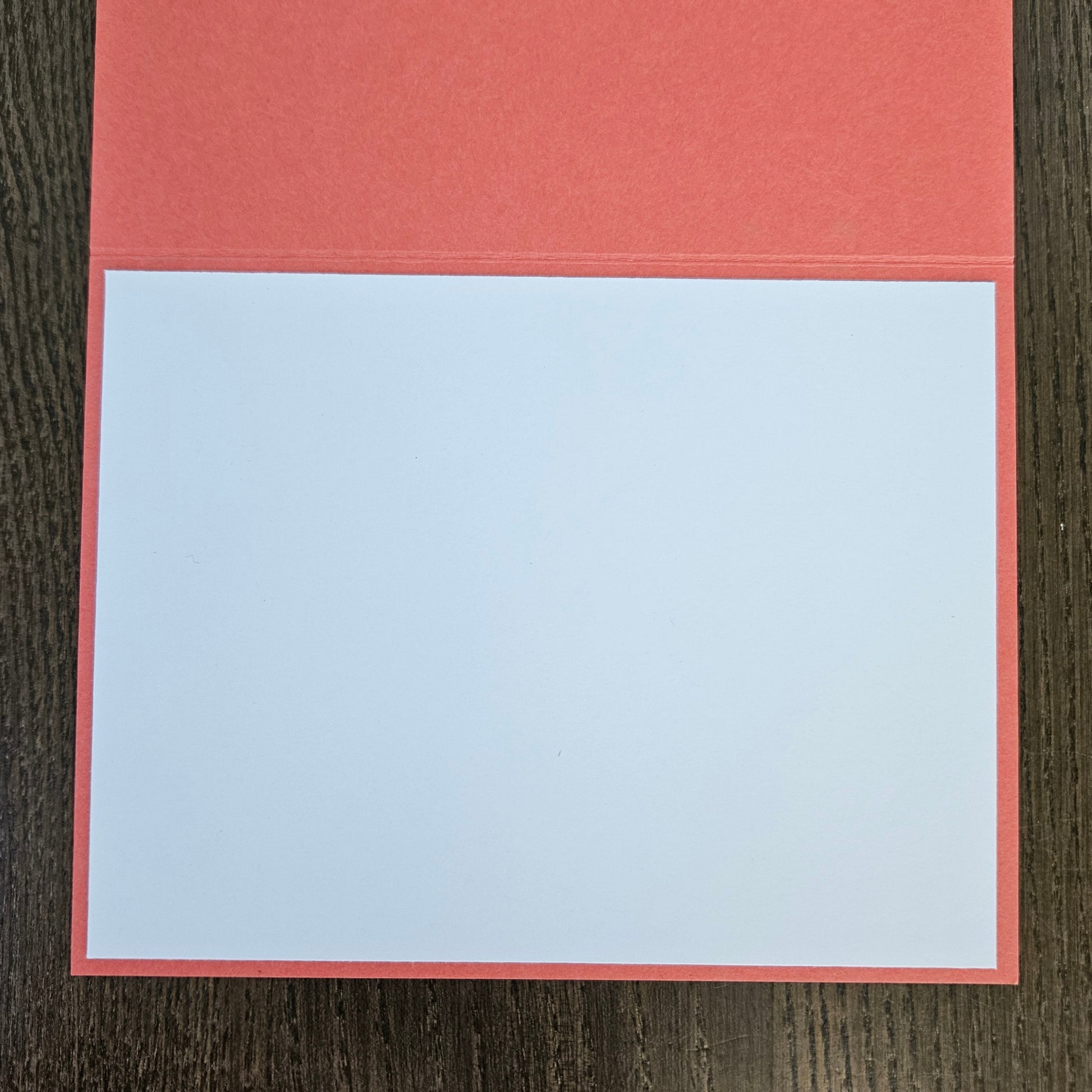 A blank white rectangular card or notepad with a coral-red border, placed on a dark brown wood-grain surface.