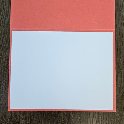 A blank white rectangular card or notepad with a coral-red border, placed on a dark brown wood-grain surface.