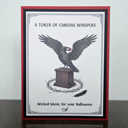 Front view of a handmade A2 gothic Halloween card featuring a raven holding a heart on a pedestal surrounded by thorns with crimson red borders. 
