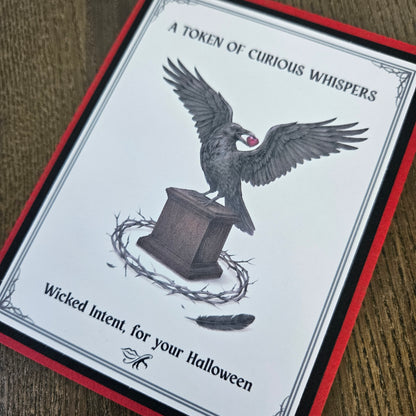 A square Halloween card or print with a white center, red border, black text reading 'A TOKEN OF CURIOUS WHISPS' and 'Wicked Intent, for your Halloween,' plus an illustration of a raven perched on a pedestal with a crown of thorns and a feather.