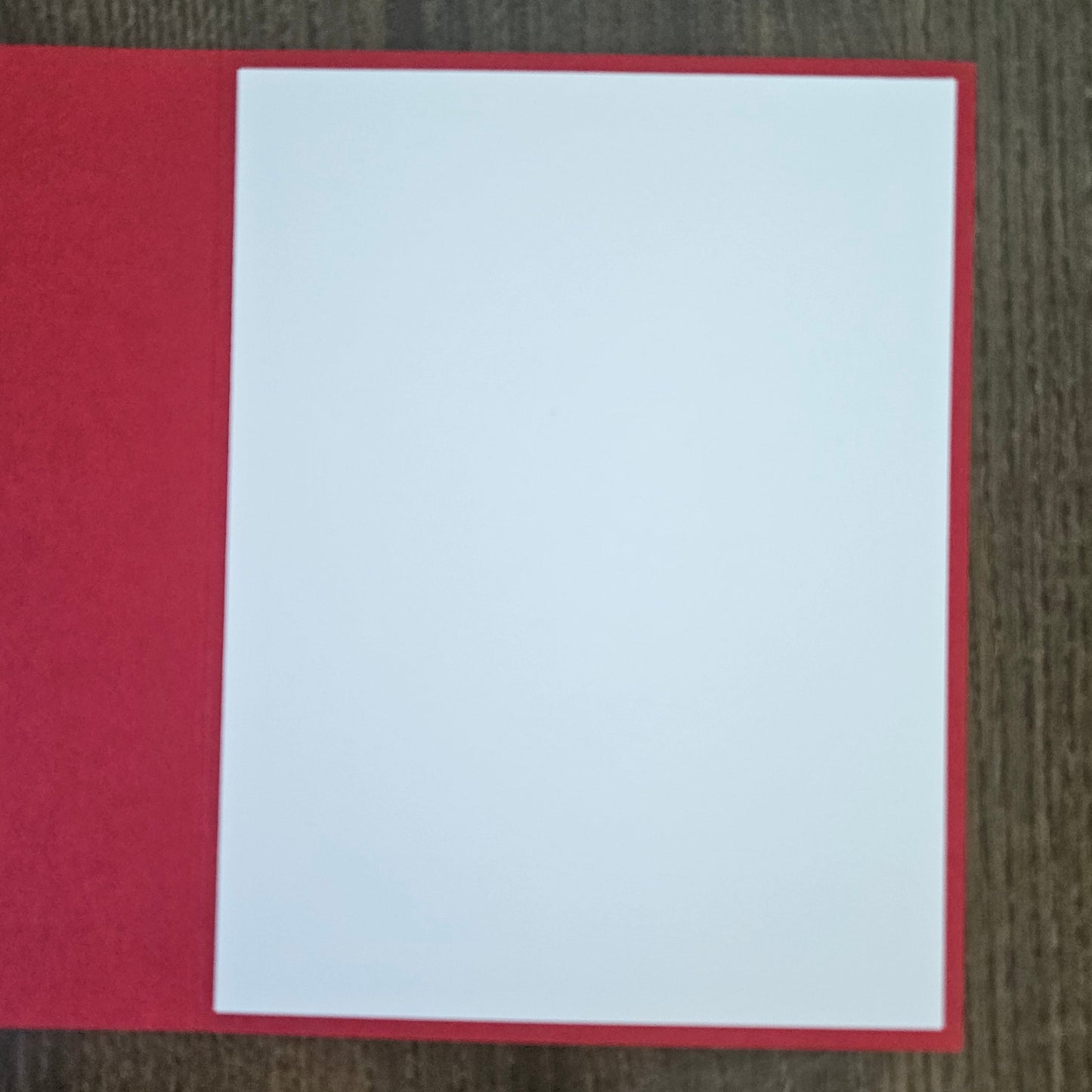 A blank white rectangular card or paper insert placed on top of a red backing, photographed from above on a dark wood surface.