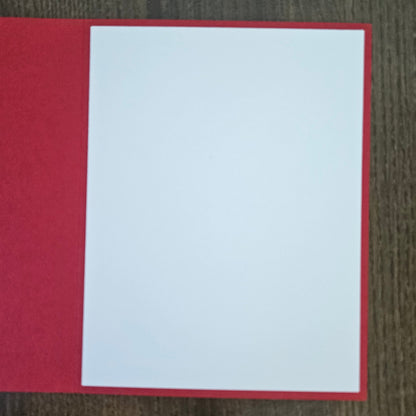 A blank white rectangular card or paper insert placed on top of a red backing, photographed from above on a dark wood surface.