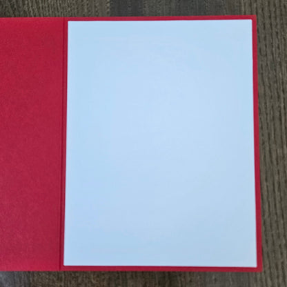 A red greeting card or notebook cover with a blank white center panel, photographed from above on a dark wood surface.