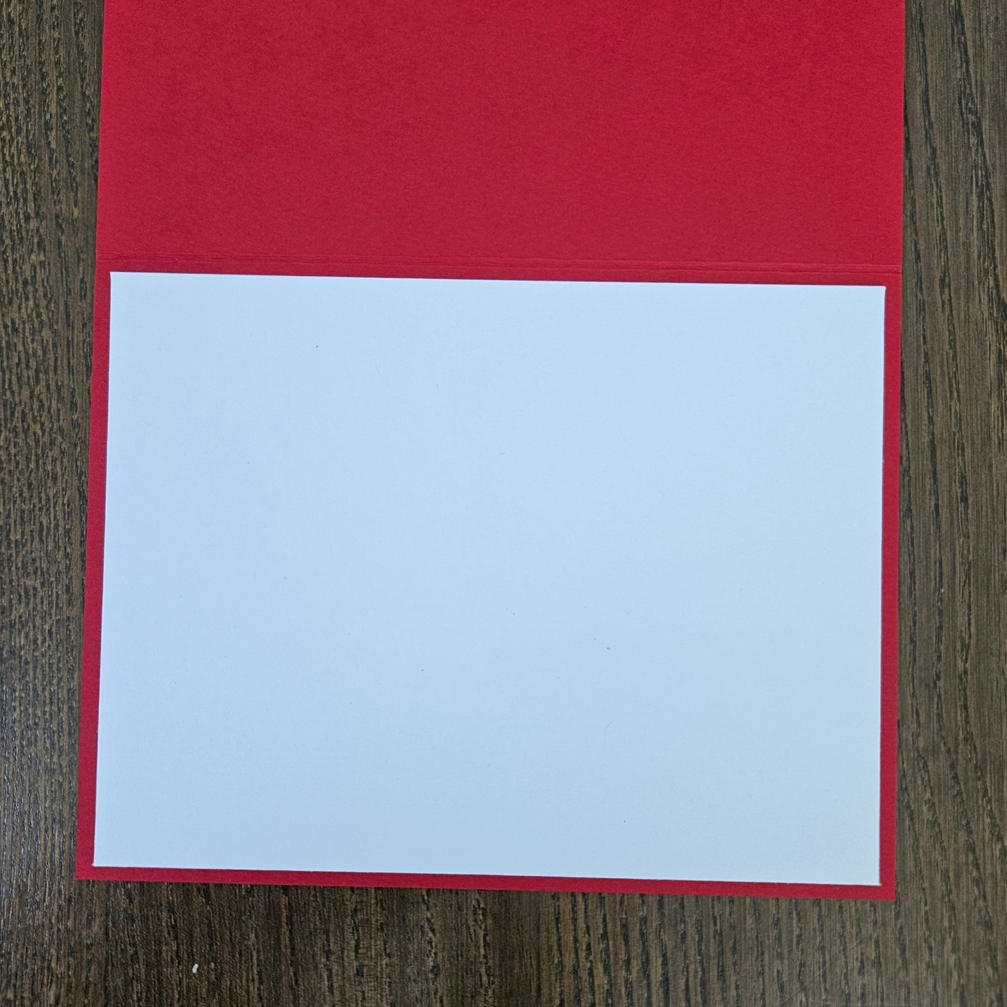 A blank white rectangular card or paper insert placed on top of a red backing sheet, photographed from above on a dark wood surface.