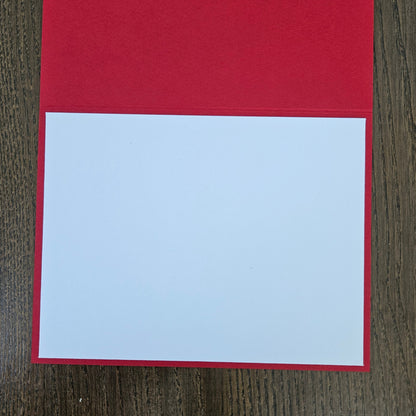 A blank white rectangular card or paper insert placed on top of a red backing sheet, photographed from above on a dark wood surface.