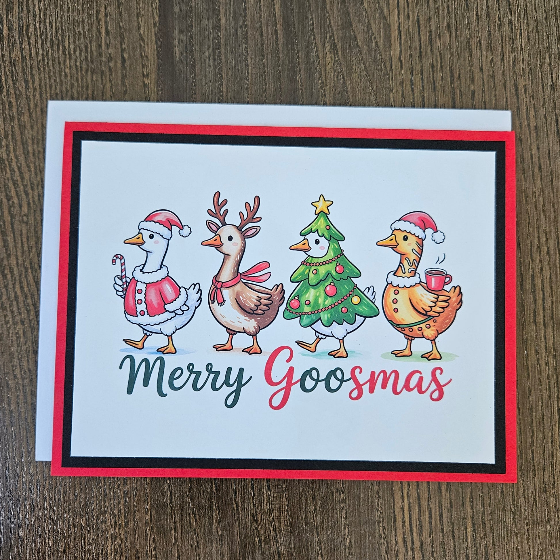 A square Christmas greeting card with a white background and colorful illustration of four festive birds around a decorated tree, with the text 'Merry Goosmas' below. The card is photographed on a brown wood surface with a white envelope behind it.