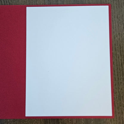 A blank white rectangular card or paper insert placed on top of a textured red sheet, photographed from above on a brown wood-grain surface.