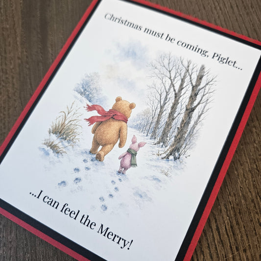 A square greeting card featuring a winter illustration of Winnie the Pooh and Piglet walking in the snow, with the text 'Christmas must be coming, Piglet.
