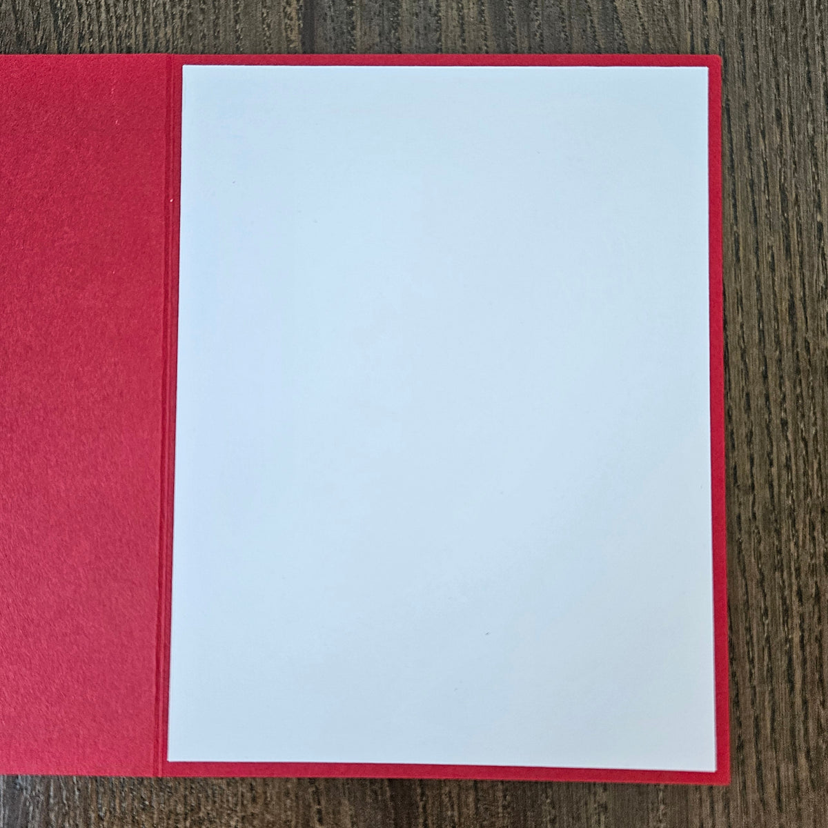A blank white card centered on a red backing, laid flat on a dark wood-grain surface.