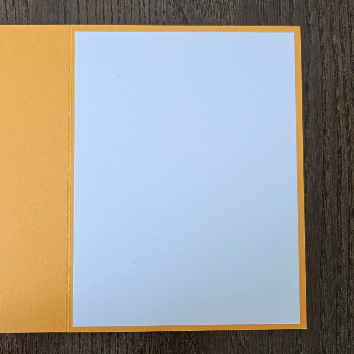 A blank white card or paper insert with a yellow-orange border, placed on a dark brown wood-grain surface.