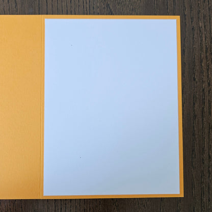 A blank white card or paper insert with a yellow-orange border, placed on a dark brown wood-grain surface.