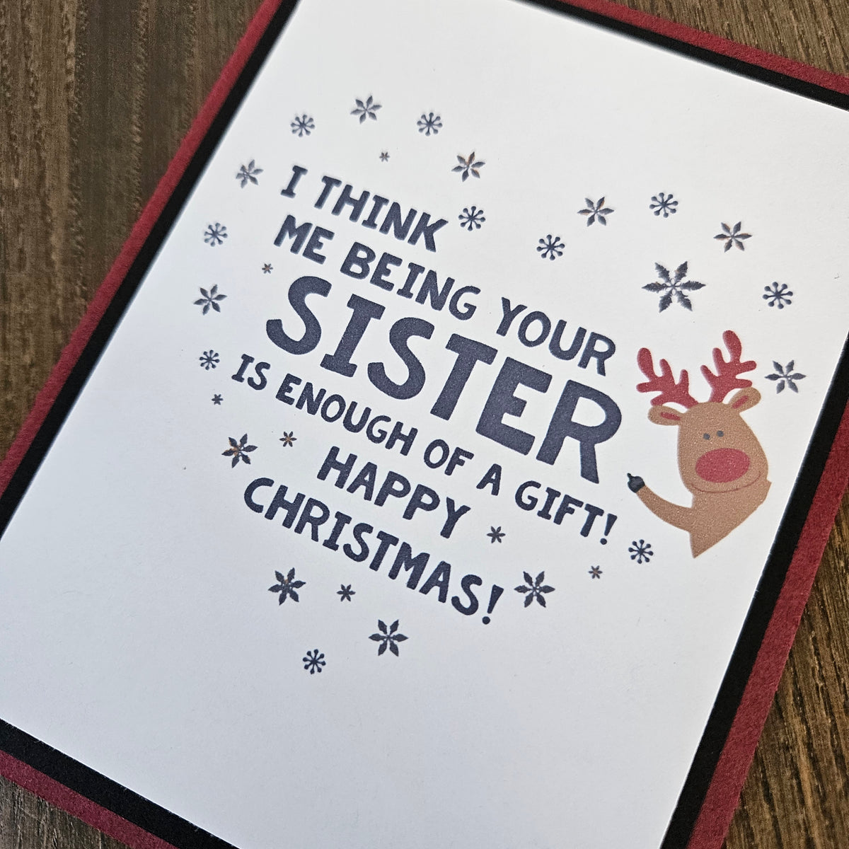 Close-up of funny sister Christmas message, red-nosed reindeer, and scattered snowflakes