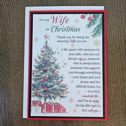 A Christmas-themed greeting card for a wife, featuring a white background with a red border, a decorated Christmas tree, wrapped gifts, and a sentimental poem, displayed on a dark wood surface.