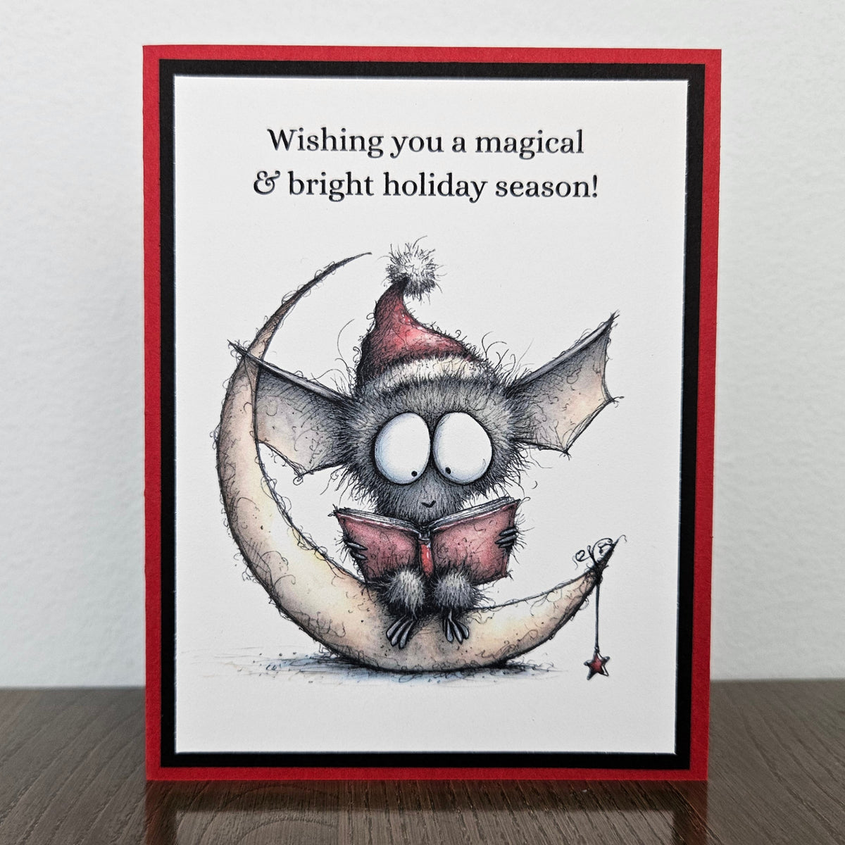 Handmade Christmas bat card with festive bat reading on a crescent moon and magical bright holiday sentiment